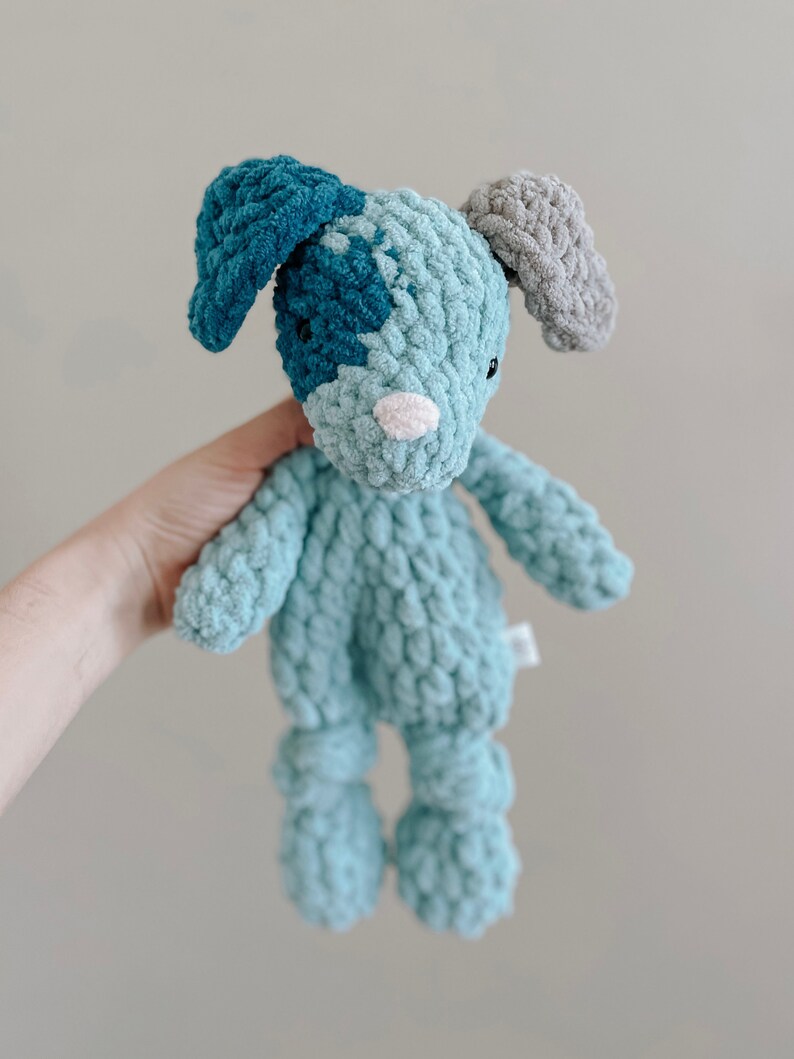 Pu&ograve; includere: Un giocattolo di peluche all'uncinetto a forma di cane. Il cane &egrave; blu e verde con le orecchie grigie. Il cane ha un naso bianco e occhi neri.