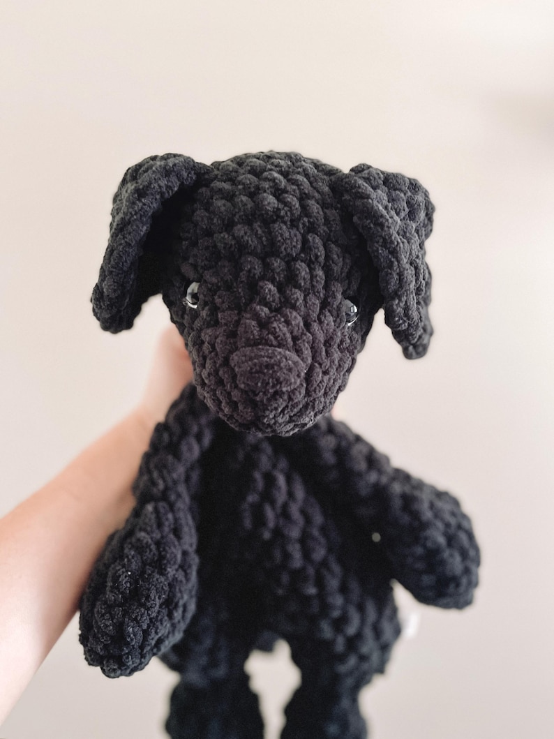 Pu&ograve; includere: Un giocattolo di peluche a forma di cane nero all'uncinetto. Il cane ha un piccolo naso nero e occhi neri.