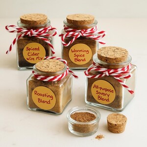 May include: Four small glass jars filled with spice blends, each with a cork lid and tied with red and white twine. The jars have labels that read "Spiced Cider Wire Mix", "Worming Spice Blend", "Roasting Blend", and "All-purpose Savory Blend". A small glass dish and a cork are also present.