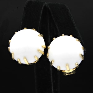 May include: A pair of white round earrings with gold accents. The earrings have a textured design around the edges.