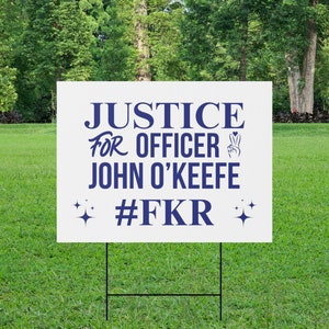 Puede incluir: Un cartel blanco con texto azul que dice "Justice for Officer John O'Keefe #FKR". El cartel está en una estaca de metal negro y está en un área cubierta de hierba.