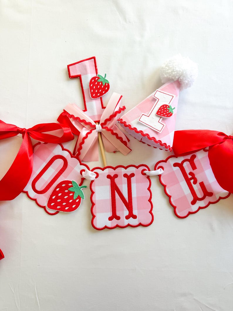 K&ouml;nnte beinhalten: Rosa-rote Geburtstagsdekorationen, darunter ein Banner mit der Aufschrift "ONE" und Erdbeeren. Enth&auml;lt die Zahl "1" und eine Partyh&uuml;tchen mit Bommel. Ideal f&uuml;r eine erste Geburtstagsfeier.