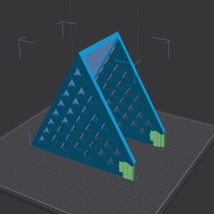 May include: A teal-colored, triangular structure with a geometric pattern of small triangles cut out of the sides. The structure has a flat base and two green rectangular supports. The background is a dark gray.