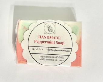 May include: Handmade Peppermint Soap bar with a green and pink swirl design. The soap is wrapped in clear plastic and has a label with the text "HANDMADE Peppermint Soap", "Net Wt. Oz 8", "scentsbyphenasa@gmail.com", and "Ingredients: Goat's Milk M&P, essentia, oi, mica".