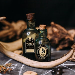 Puede incluir: Dos botellas de boticario antiguas de vidrio con tapones de corcho. Una botella tiene una etiqueta que dice "UNFILTERED POISON, Finest Quality". La otra botella tiene una etiqueta que dice "RAVEN'S CURSE, Finest Quality, Apothecary".