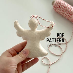 Könnte beinhalten: Ein weißer Filzengel-Anhänger mit einer rot-weißen Schnur. Der Anhänger wird in einer Hand gehalten. Der Text "PDF PATTERN + PHOTO AND TEXT INSTRUCTIONS" ist auf dem Bild zu sehen.