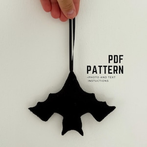 May include: A black felt bat ornament with a ribbon for hanging. The bat has outstretched wings and a pointed tail. Text on the right reads "PDF PATTERN + PHOTO AND TEXT INSTRUCTIONS".