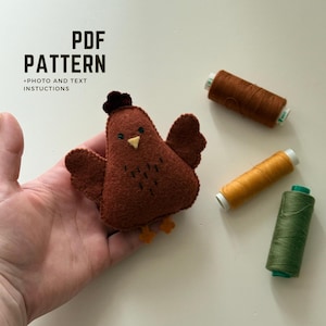 May include: A handmade felt chicken with a dark brown body, wings, and a small comb. The chicken has a yellow beak and orange feet. The image includes the text "PDF PATTERN + PHOTO AND TEXT INSTRUCTIONS" and three spools of thread.