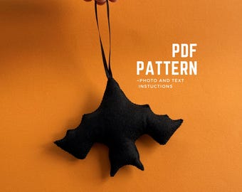 May include: A black felt bat ornament with a black ribbon for hanging. The bat has outstretched wings and is suspended against an orange background. Text on the image reads "PDF PATTERN + PHOTO AND TEXT INSTRUCTIONS."