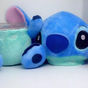 May include: Blue and light blue plush toy of a cartoon character with large ears and big eyes. The toy is holding a clear glass jar.