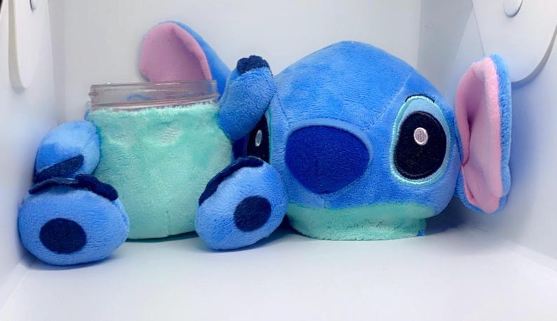 May include: Blue and light blue plush toy of a cartoon character with large ears and big eyes. The toy is holding a clear glass jar.