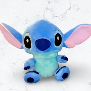 May include: A blue and pink plush toy of Stitch from the Disney movie Lilo & Stitch. The toy is sitting with its legs crossed and has a big, friendly smile.