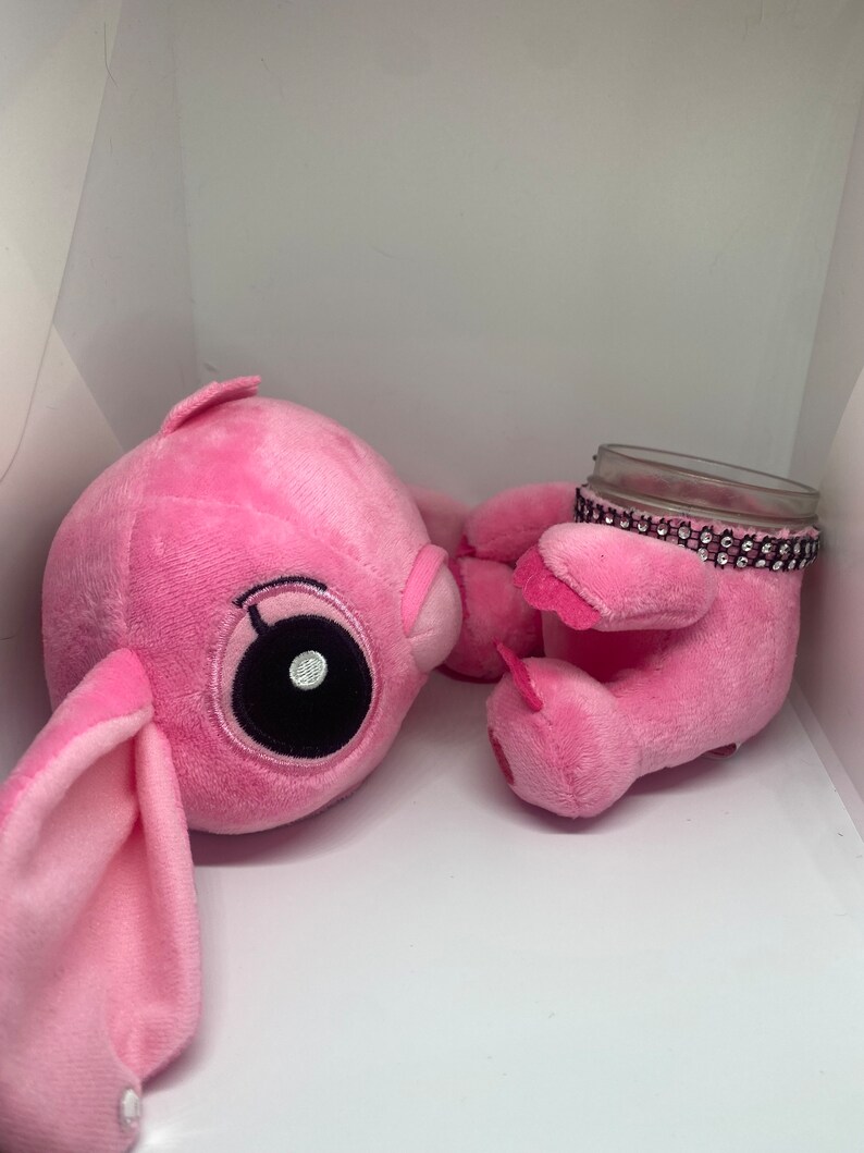 May include: Two pink plush toys, one with large eyes and floppy ears, the other holding a clear glass jar with a pink rhinestone trim.