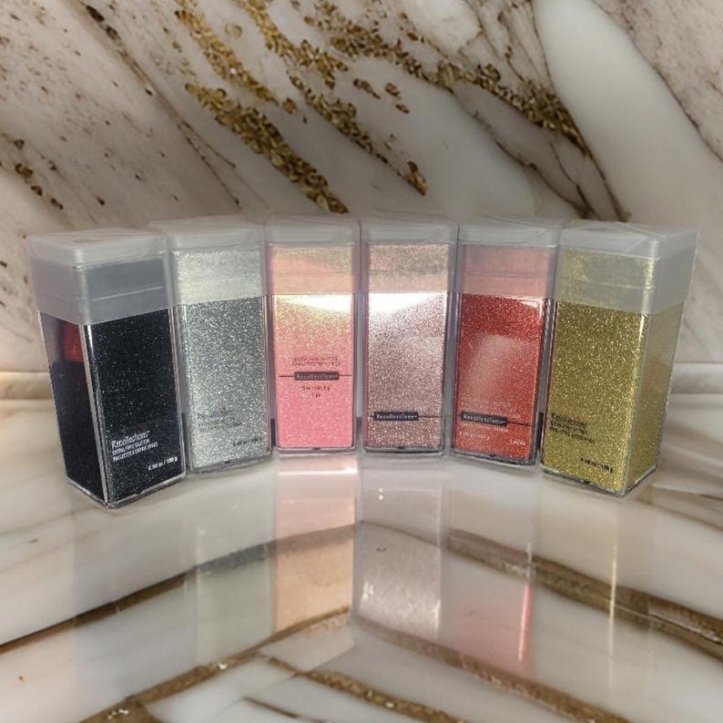 May include: Seven small clear plastic containers filled with different colored glitter. The containers are labeled with the word "Beautifullover" and the color of the glitter. The colors are black, silver, pink, rose gold, red, and gold.