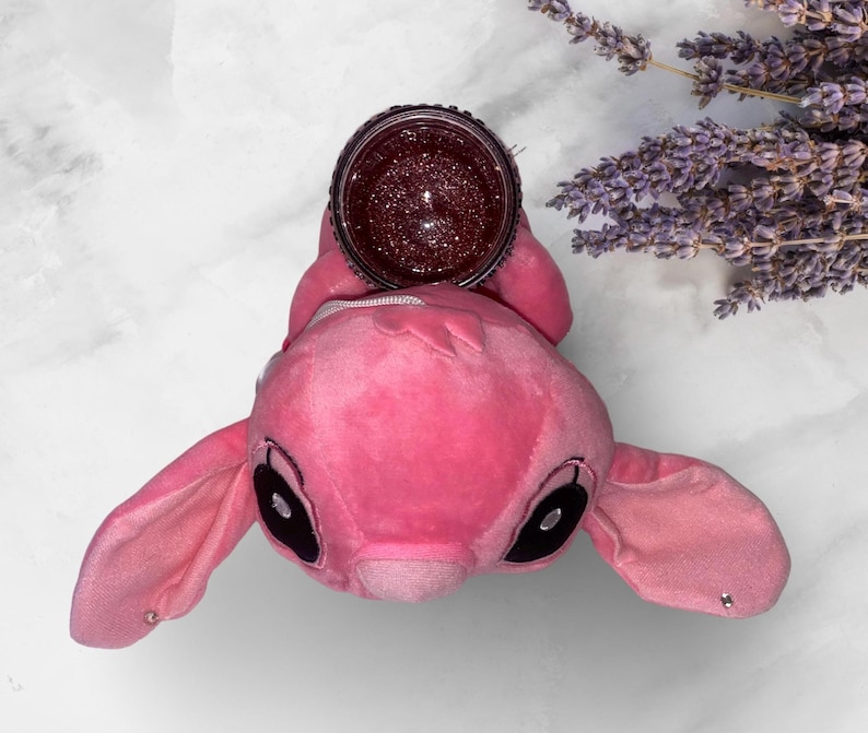 May include: Pink plush toy shaped like a cartoon character with large ears and black eyes. The toy is holding a clear jar with a glittery pink substance inside.
