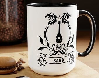 May include: White ceramic mug with a black rim and handle. The mug features a black and white design of a lute, two dragons, and a dice with the word "BARD" on a banner.