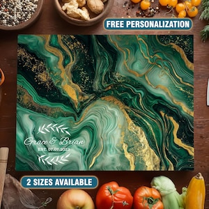 May include: A rectangular cutting board with a green and gold marble design. The board has the text "Grace & Brian" and "Est. 07.07.2023" in white. The words "2 sizes available" are also visible. Knives and fresh produce surround the board.