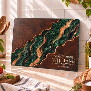 May include: A rectangular glass cutting board featuring a dark wood grain pattern on the left and right sides, separated by a central flowing river design of marbled green and metallic copper. The text reads Emily & Henry WILLIAMS est. 11.11.2026.