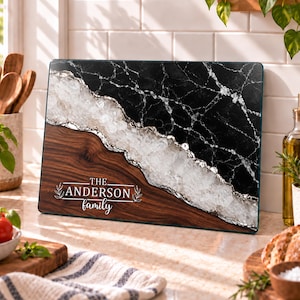 May include: A rectangular glass cutting board featuring a split design of black marble and dark wood grain, separated by a textured white crystalline band. The text THE ANDERSON family is printed in white with decorative leaf accents.