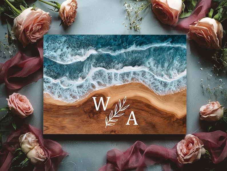 May include: A wooden sign with a resin ocean design. The top half shows blue and white waves, leading to a brown beach. White letters "W A" and a leaf design are in the center. Pink roses and burgundy fabric surround the sign.