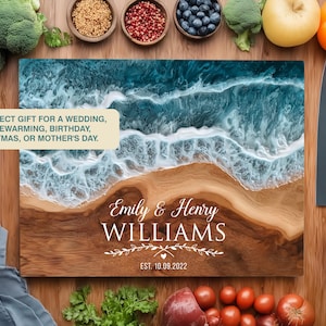 May include: A wooden chopping board with a beach design, featuring a wave pattern in blue and white resin. The board is personalised with the names "Emily & Henry Williams" and the date "EST. 10.09.2022". Two knives are placed to the right. The text reads "THE PERFECT GIFT..."