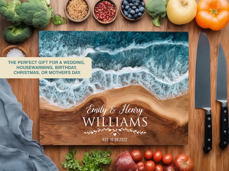May include: A wooden chopping board with a beach design, featuring a wave pattern in blue and white resin. The board is personalised with the names "Emily & Henry Williams" and the date "EST. 10.09.2022". Two knives are placed to the right. The text reads "THE PERFECT GIFT..."