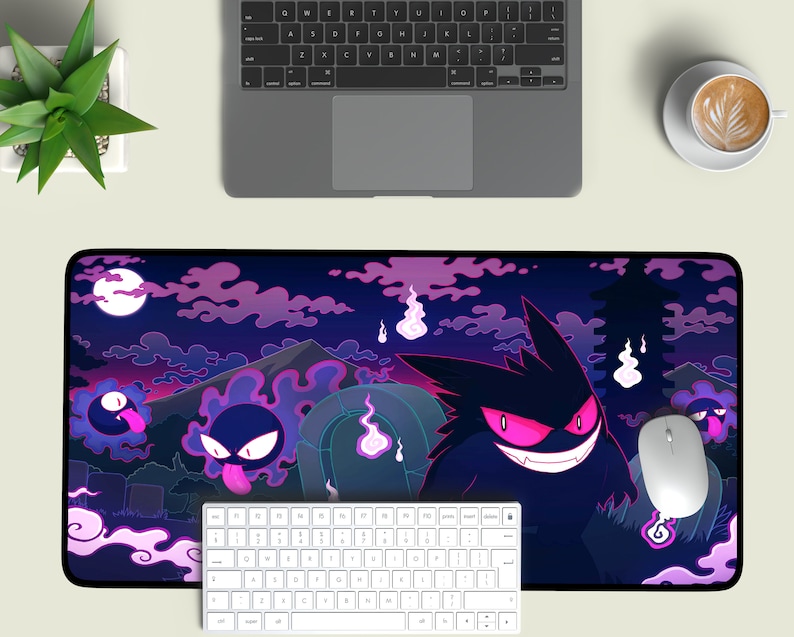 May include: A black and purple gaming mouse pad with a design of a cartoon ghost with glowing pink eyes. The ghost is surrounded by other smaller ghosts and clouds. The mouse pad is on a white surface with a keyboard and a coffee cup.