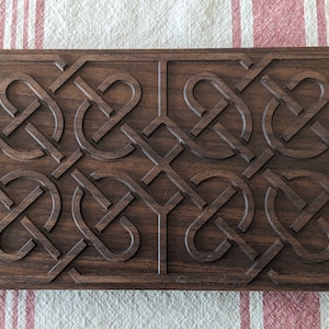 Op de afbeelding: Een donkerbruine houten doos met een gegraveerd Keltisch knoopontwerp. De doos is rechthoekig en heeft een glad oppervlak.