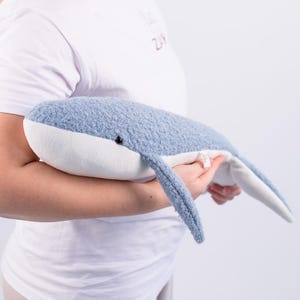 Peut inclure: Une peluche en forme de baleine, de couleur bleu et blanc. La baleine a un corps bleu clair texturé et un ventre blanc. Elle présente un petit œil noir et une queue incurvée. Le jouet est doux et câlin, pour les enfants.