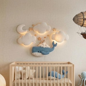 May include: A nursery scene with a wooden crib, a whale-shaped wall decoration, and a blimp-shaped light fixture. A bookshelf displays globes and nautical decor. A round paper lantern and a woven basket with stuffed animals complete the room.