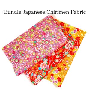 以下が含まれることがあります： 日本の縮緬生地の正方形が3枚セットになっています。生地は柔らかく、絹のような質感で、伝統的な花柄が施されています。正方形はピンク、赤、黄色の色合いです。