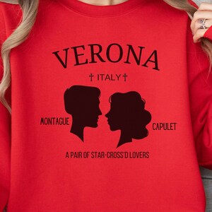 May include: Red sweatshirt with a black graphic design that says "VERONA + ITALY +" with silhouettes of a man and woman and the text "MONTAGUE CAPULET A PAIR OF STAR-CROSS'D LOVERS"