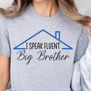 Puede incluir: Una camiseta gris con un gráfico de casa azul y el texto "Hablo con fluidez Big Brother".
