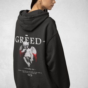 May include: Black hooded sweatshirt with a white graphic print of an angel with red blood dripping from its wings. The text "GREED+ a deadly sin" is printed below the angel. The text "plunges a man deep into the mire of this world, so that he makes it to be his god." is printed below the text "a deadly sin".