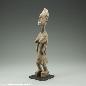 Puede incluir: Una escultura de madera de una figura femenina con una cabeza estilizada y una mano levantada. La escultura está tallada en un color marrón claro y tiene un acabado liso y pulido.