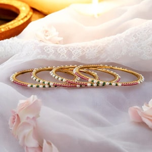 May include: Set of five gold bangles with pink and green beads and white pearls.