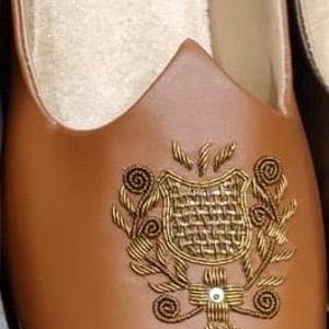 May include: Brown leather slip-on shoe with an embroidered gold design on the vamp. The shoe has a pointed toe and a soft, light-colored interior. A decorative shoe for special occasions.