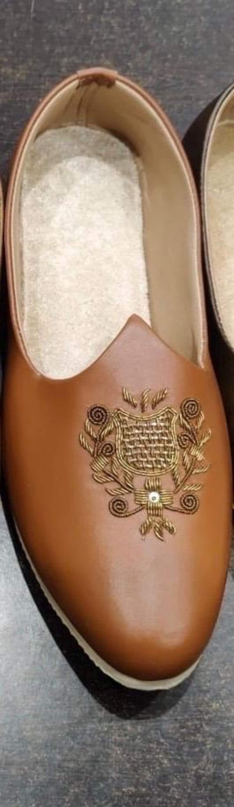 May include: Brown leather slip-on shoe with an embroidered gold design on the vamp. The shoe has a pointed toe and a soft, light-colored interior. A decorative shoe for special occasions.