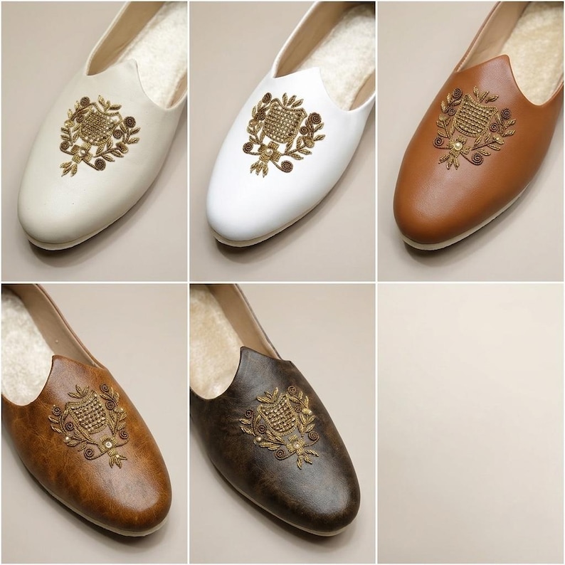 May include: Six pairs of slip-on shoes in various colors: cream, white, light brown, medium brown, and dark brown. Each shoe features an embroidered gold crest design on the vamp and a soft, light-colored interior lining.