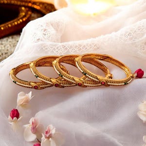 May include: Four gold bangles with white pearl and green accents. Each bangle has a red stone in the center.