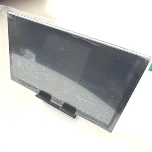 Può includere: Uno schermo nero con una copertura protettiva in plastica. Lo schermo è montato su un supporto nero.