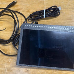May include: A black, rectangular, framed screen with a black cable attached. The screen has a row of white lights along the top edge.