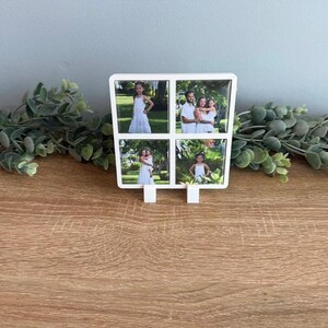 May include: A white square photo frame with four distinct compartments, each displaying a different outdoor photograph. The frame is supported by two small white feet at the base, allowing it to stand upright on a flat surface.