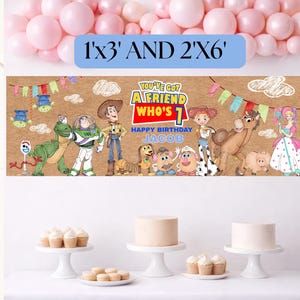May include: A rectangular birthday banner featuring Toy Story characters on a tan background with colorful bunting. The text reads: YOU'VE GOT A FRIEND WHO'S 1, HAPPY BIRTHDAY, JACOB. A blue label above displays the dimensions 1'x3' AND 2'X6'.