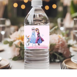 May include: A clear plastic water bottle with a pink label featuring cartoon characters from the movie Frozen. The label includes the text "Sophia's 2nd birthday". The bottle is on a table set for a party.