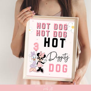 Op de afbeelding: Een ingelijste print met een roze en wit ontwerp met de woorden "HOT DOG" en "Diggity DOG". Het nummer "3" wordt weergegeven met een ballon, en de stripfiguren Minnie en Daisy Mouse zijn ook afgebeeld.