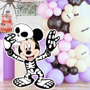 Peut inclure: Scène de fête d'Halloween avec une découpe de Mickey Mouse squelette tenant un crâne. Une arche de ballons noirs, blancs et violets est en arrière-plan. Un gâteau à plusieurs niveaux et des décorations d'araignées complètent le décor festif.