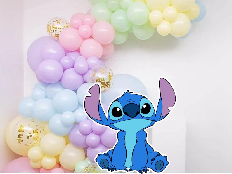 May include: A blue cartoon character with large eyes and a big smile, sitting in front of a pastel balloon arch. The balloons are in shades of pink, purple, blue, and yellow.