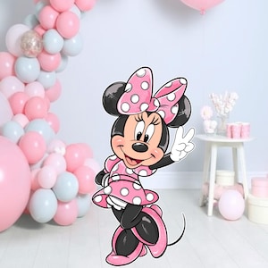 Op de afbeelding: Een cartoon illustratie van Minnie Mouse in een roze polkadot jurk en strik, die een vredesteken geeft. De achtergrond toont een ballonnenboog in roze, witte en zilveren tinten, met extra roze ballonnen en feestversieringen.