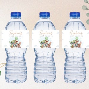 Op de afbeelding: Drie doorzichtige plastic waterflessen met etiketten waarop "Sophia's Baby Shower" staat en een cartoon-dinosaurus en andere personages te zien zijn.